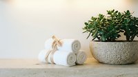 Spa wellness setup with rolled white towels, wooden massage tool and green succulent plant in stone bowl on natural shelf for relaxation and self-care.