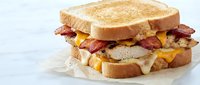 Delicious bacon egg cheese sandwich on toasted bread with melted cheese and crispy bacon strips, breakfast comfort food meal on white background isolated.