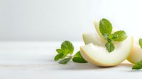 Fresh honeydew melon slices with vibrant mint leaves on white wooden surface, creating refreshing summer food composition for healthy eating concepts.