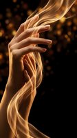 Elegant female hands with flowing golden silk fabric and sparkling particles on dark background for luxury beauty and skincare concepts.