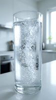 Clear glass filled with sparkling water showing effervescent bubbles rising in modern kitchen setting for hydration and wellness concepts.