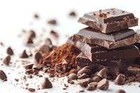 Stack of dark chocolate pieces with cocoa powder, chocolate chips and coffee beans scattered on white background, macro food photography for confectionery marketing.