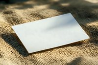 Blank white paper sheet on natural burlap textile background with soft shadows and copy space for text or design mockup presentation.