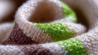 Macro view of natural linen fabric texture with brown and green stripes pattern. Close up of woven textile material showing detailed fiber structure.