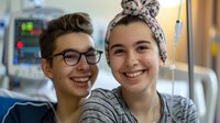Young cancer patient with head scarf smiling with teenage friend in hospital room, medical equipment visible in background, showing support and positivity during treatment.
