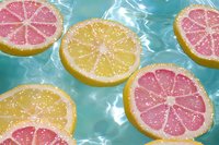Sliced citrus fruits floating in turquoise water with grapefruit and lemon halves, ideal for summer beverage and wellness designs.