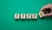 Hand placing wooden cube with light bulb icon next to question mark blocks on green background representing problem solving and creative thinking process.