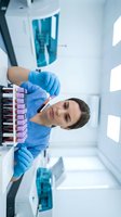 Female laboratory technician in blue gloves examining blood sample test tube in modern medical lab for healthcare research and diagnostic testing.