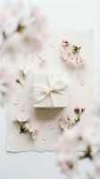 Elegant white gift box tied with a ribbon surrounded by delicate pink cherry blossoms on textured paper, soft romantic flatlay.