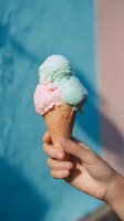 Refreshing mint and strawberry ice cream cone held against vibrant blue wall, perfect for summer food marketing and dessert promotions.