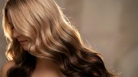 Young woman with long wavy blonde hair in soft natural lighting showcasing healthy shiny locks for beauty and haircare concepts.