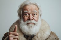 Cheerful senior man with natural white beard and fur coat showing thumbs up against light background. Positive aging concept with genuine smile.