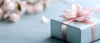 Elegant gift box wrapped in mint paper with pink ribbon and delicate cherry blossom on gray background, romantic celebration concept for special occasions.