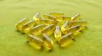 Golden omega-3 fish oil capsules scattered on green textile surface for health and wellness supplement nutrition concept.