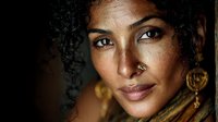 Young mixed-race woman with curly hair and nose piercing in warm golden lighting. Portrait photography with ethnic jewelry and natural makeup for beauty campaigns.