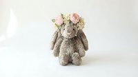 Adorable gray plush bunny rabbit wearing delicate pink rose flower crown sits against soft neutral background for nursery decor and baby photography.