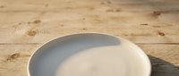 Empty white ceramic plate on wooden surface with natural sunlight casting soft shadows, suitable for food styling and culinary content.