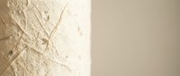 Textured cream wall surface with natural fiber patterns and soft lighting creating warm shadows for interior design and architectural backgrounds.