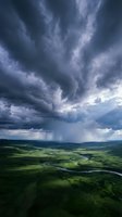 Dramatic storm clouds gather over lush green valley with winding river below, showcasing nature's power and atmospheric weather conditions for environmental and landscape projects.