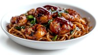 Glazed meatballs with noodles in savory sauce garnished with fresh herbs served in white bowl for restaurant menu and cooking content.