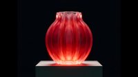 Red glass vase with ribbed texture glowing on illuminated platform against black background for luxury home decor and interior design projects.