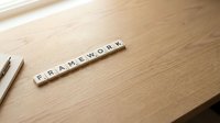Wooden letter tiles spelling FRAMEWORK on natural wood desk surface with pencils, business planning and strategy concept for presentations.