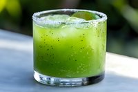 Fresh green cocktail with salt rim and lime garnish in rocks glass on white surface, refreshing summer drink with crushed ice and natural ingredients.