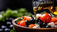 Fresh Mediterranean salad with olive oil being poured over colorful vegetables, olives, and cheese in wooden bowl for healthy cooking and dining.