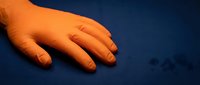 Young child's hand resting on dark blue fabric surface, warm orange lighting, studio shot for parenting, childcare, family concepts.
