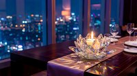 Elegant dining table with crystal candle holder and wine glasses overlooking illuminated city skyline at night through large windows creating romantic atmosphere.