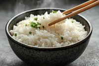 Steaming hot white rice garnished with fresh chopped chives served in rustic ceramic bowl with wooden chopsticks against dark background with rising steam.