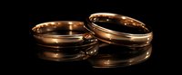 Elegant gold wedding bands with subtle reflections on dark surface, symbolizing eternal commitment and matrimonial bond. Classic jewelry photography for wedding themes.