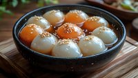 Traditional Asian glutinous rice balls tang yuan dessert with sesame seeds in sweet syrup served in black ceramic bowl on wooden table for celebrations.