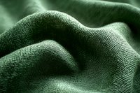 Green textured fabric with gentle folds and waves creating an abstract landscape-like surface with detailed woven pattern visible in dramatic lighting.
