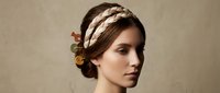 Young Caucasian woman with elegant braided updo hairstyle and decorative buttons hair accessory, soft neutral background, beauty and fashion concept.