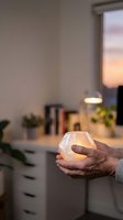 Person holding glowing LED candle in modern home interior at sunset, creating warm ambient lighting for relaxation and decoration purposes.