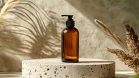 Amber glass pump bottle on concrete podium with palm shadow and dried pampas grass. Minimalist cosmetic packaging mockup for natural skincare products.