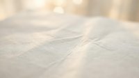 Soft beige linen fabric texture with natural wrinkles and folds creating gentle shadows and highlights for textile and interior design backgrounds.