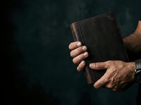 Close-up of male hands holding worn leather wallet against dark background. Suitable for finance, savings, banking, and lifestyle content.