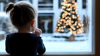 Young child gazing through window at illuminated Christmas tree with bokeh lights on snowy winter evening, creating nostalgic holiday atmosphere.
