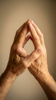 Elderly hands pressed together in prayer or meditation gesture against warm beige background showing wisdom, spirituality and peaceful contemplation.