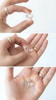 Hands holding clear crystal gemstone with rainbow light reflections creating prismatic effects on white background for jewelry and luxury concepts.