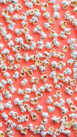 Fresh white popcorn kernels scattered across vibrant coral background for movie night snacks, cinema treats, entertainment food concepts and kitchen designs.