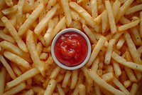 Crispy golden french fries arranged around white ceramic bowl with bright red ketchup sauce, overhead view showing texture and seasoning of fried potatoes.