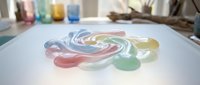 Colorful watercolor paint swirls blending on white paper in artist studio workspace with brushes and paint tubes creating abstract rainbow pattern.