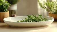 Fresh green herbs in white ceramic bowl on wooden table with potted plants in background for cooking and culinary preparation.