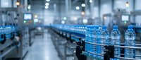 Plastic water bottles moving along conveyor belt in modern beverage manufacturing facility with industrial equipment and blurred background for production and packaging concepts.