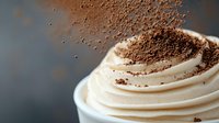 Creamy whipped topping swirled in peaks with chocolate powder sprinkled on top against dark background, macro food photography for dessert menu or recipe blog.