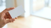 Close-up of adult hand holding blank white card in bright interior space with natural window light, suitable for business branding and marketing mockups.