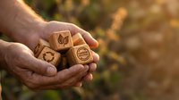 Farmer holding wooden blocks with sustainability and organic farming symbols in cupped hands outdoors, representing eco-friendly agriculture and environmental responsibility.